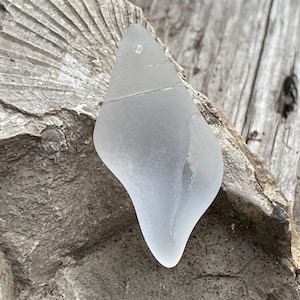 May include: A smooth, white sea glass pendant with a hole at the top for hanging. The glass is translucent and has a slightly cloudy appearance.