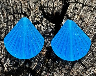 May include: Two blue glass sea shell shaped earrings with a textured surface.