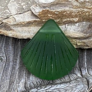 May include: A green glass sea shell pendant with a ribbed design. The pendant is sitting on a piece of driftwood.