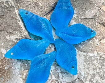 May include: Six teal blue glass sea shells arranged in a star shape on a gray stone background.