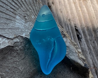 May include: A blue glass sea glass piece shaped like a seashell with white swirls inside.