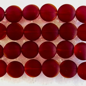 May include: Twenty-four round, red glass beads. The beads are smooth and have a slight sheen.