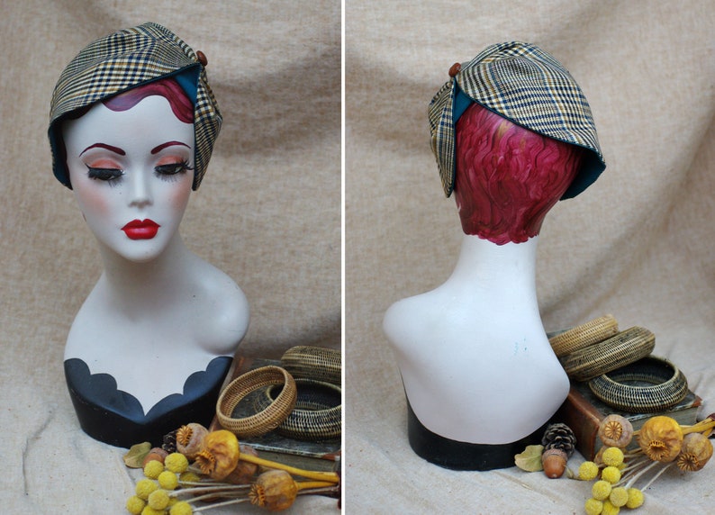 May include: A brown and black plaid hat with a teal blue trim and a brown button on top. The hat is on a mannequin head with red hair.