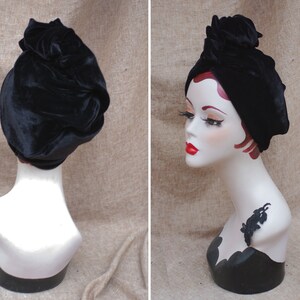 May include: A black velvet turban style hat with a knotted top. The hat is on a white mannequin head.