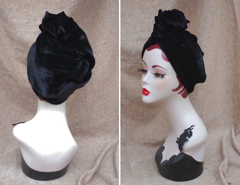 May include: A black velvet turban style hat with a knotted top. The hat is on a white mannequin head.