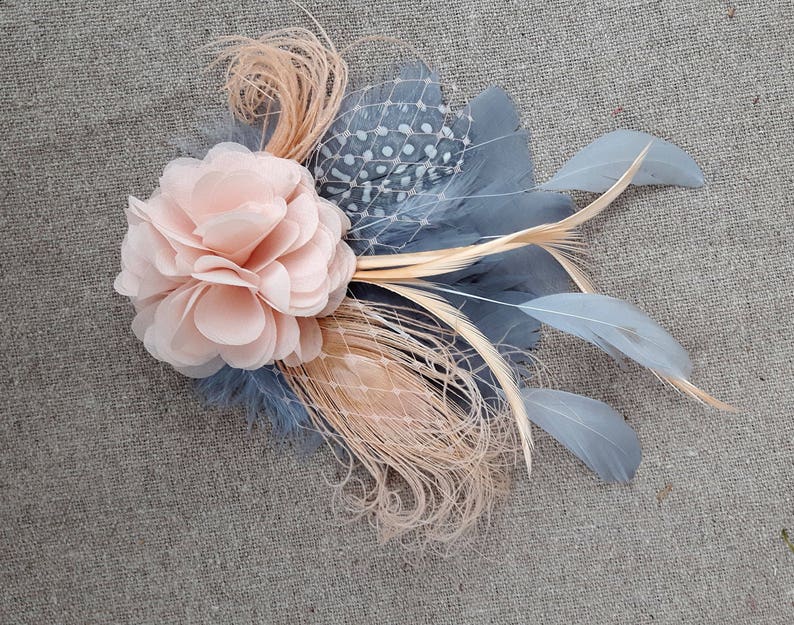 Peut inclure: Une fleur en tissu rose p&acirc;le avec un embellissement en plumes et filet gris et beige.