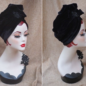 May include: A black velvet turban with a black beaded embellishment. The turban is worn on a mannequin with a black lace trim around the neck.