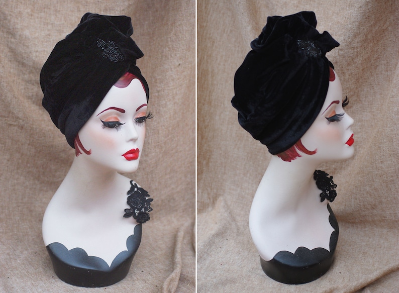 May include: A black velvet turban with a black beaded embellishment. The turban is worn on a mannequin with a black lace trim around the neck.