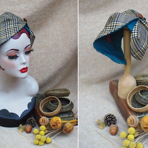 May include: A plaid and teal fabric hat with a bow on top. The hat is displayed on a wooden mannequin and a book with wicker baskets.