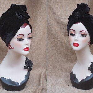 May include: A black velvet turban with a black beaded embellishment. The turban is worn on a white mannequin head with a black lace accent on the shoulder.