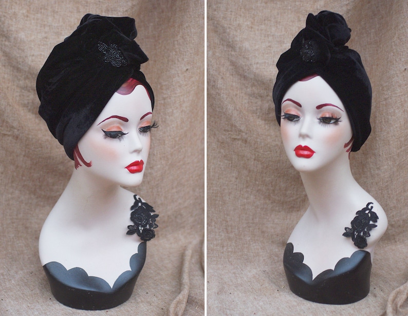 May include: A black velvet turban with a black beaded embellishment. The turban is worn on a white mannequin head with a black lace accent on the shoulder.