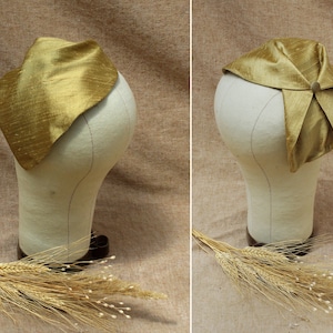 May include: A gold silk scarf is folded and tied on a white mannequin head. The scarf is a triangular shape and has a subtle sheen. The mannequin is on a brown background.