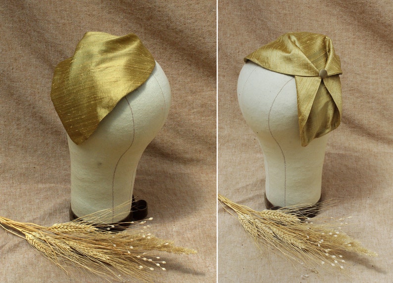May include: A gold silk scarf is folded and tied on a white mannequin head. The scarf is a triangular shape and has a subtle sheen. The mannequin is on a brown background.