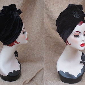 May include: A black velvet turban with a black beaded embellishment. The turban is worn on a white mannequin head.