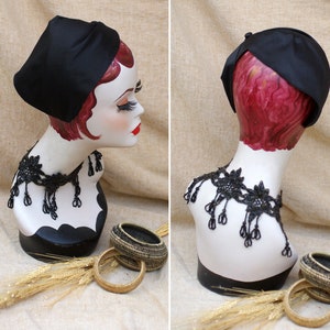 May include: A black satin hat with a rounded crown and a wide brim. The hat is on a mannequin wearing a black lace necklace.