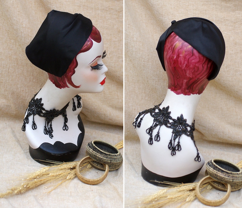 May include: A black satin hat with a rounded crown and a wide brim. The hat is on a mannequin wearing a black lace necklace.