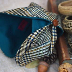 May include: A teal blue and plaid fabric hat with a brown button on the side. The hat is folded and the inside of the hat is visible.