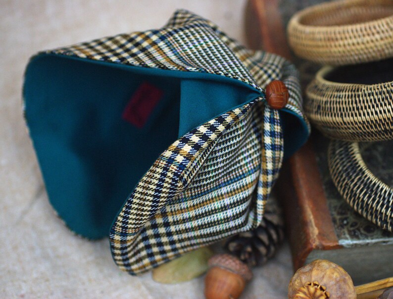 May include: A teal blue and plaid fabric hat with a brown button on the side. The hat is folded and the inside of the hat is visible.