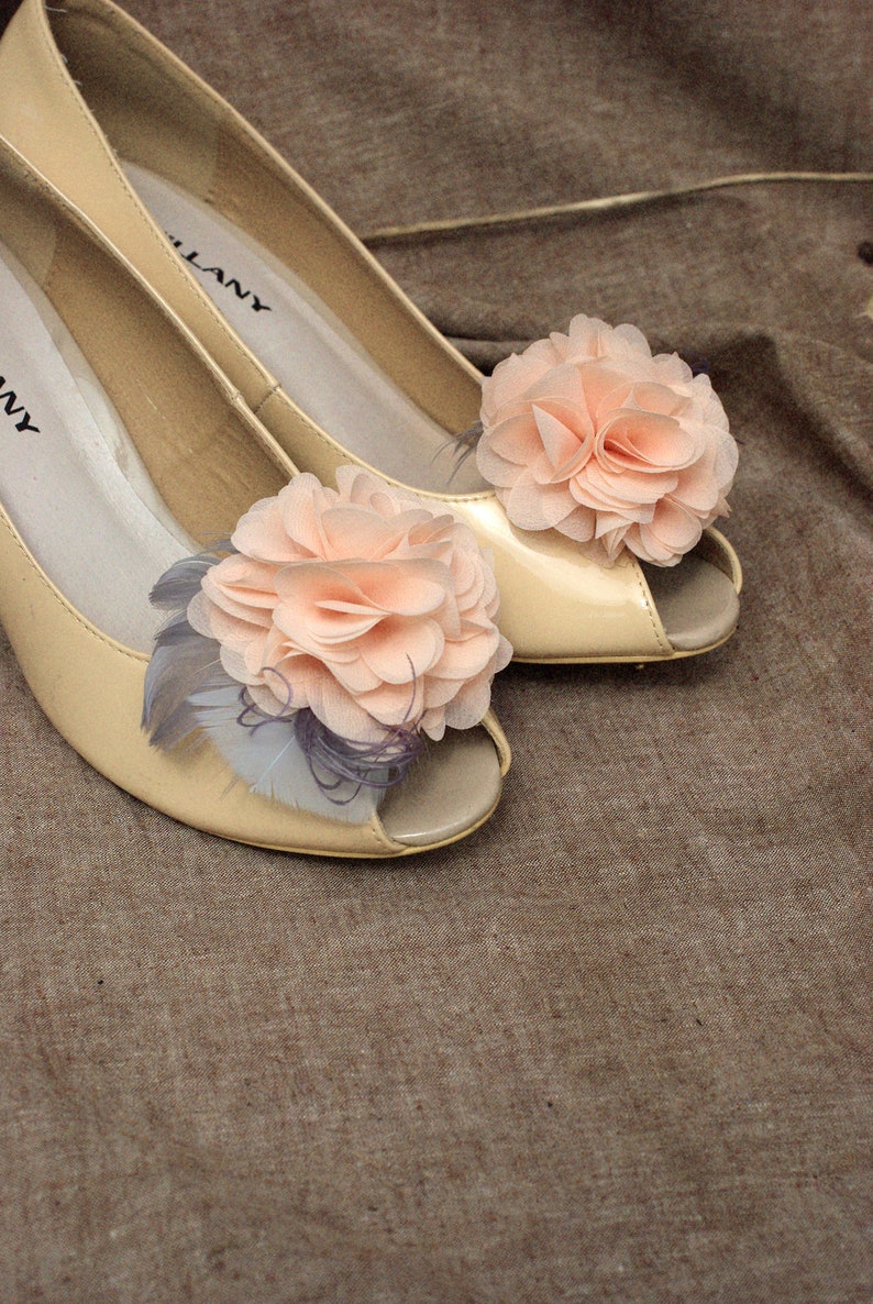 Peut inclure: Une paire de chaussures &agrave; talons beiges avec un bout ouvert et une d&eacute;licate fleur en embellissement sur chaque chaussure. Les fleurs sont de couleur rose clair et sont faites de tissu.