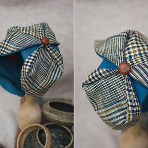 May include: A blue and brown plaid fabric hat with a teal lining and a wooden button on top.