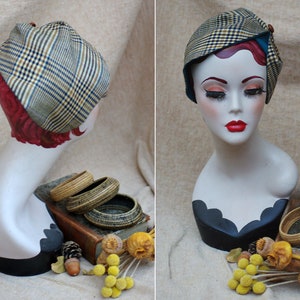 May include: A mannequin head wearing a brown and beige plaid hat with a blue trim. The hat is tilted slightly to the side. The mannequin is wearing a black and white patterned dress.