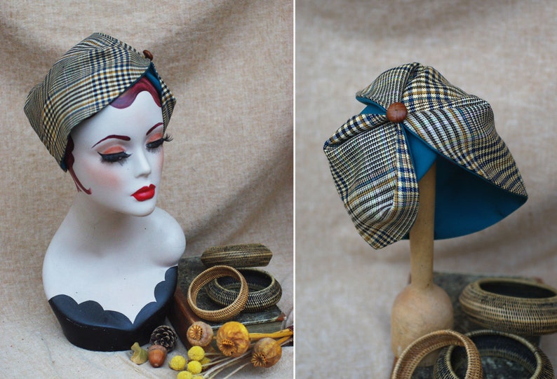 May include: A brown and black plaid hat with a teal lining and a brown button on top. The hat is on a wooden stand.