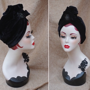 May include: A black velvet turban with a black beaded embellishment. The turban is worn on a mannequin with a black lace accent.