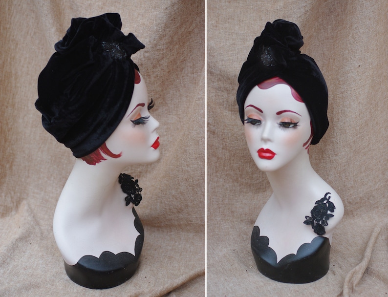 May include: A black velvet turban with a black beaded embellishment. The turban is worn on a mannequin with a black lace accent.