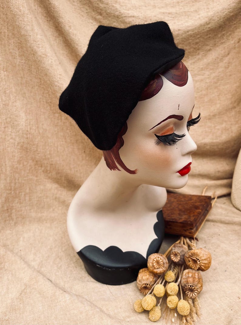 K&ouml;nnte beinhalten: Ein schwarzer Filz-Barett auf einem Mannequin-Kopf. Das Mannequin hat rote Haare und tr&auml;gt Make-up. Der Barett sitzt auf einem schwarz-wei&szlig;en St&auml;nder.