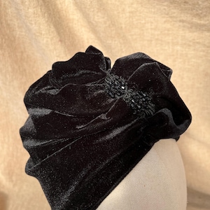 May include: A black velvet hat with a large, ruffled bow and a black beaded embellishment.