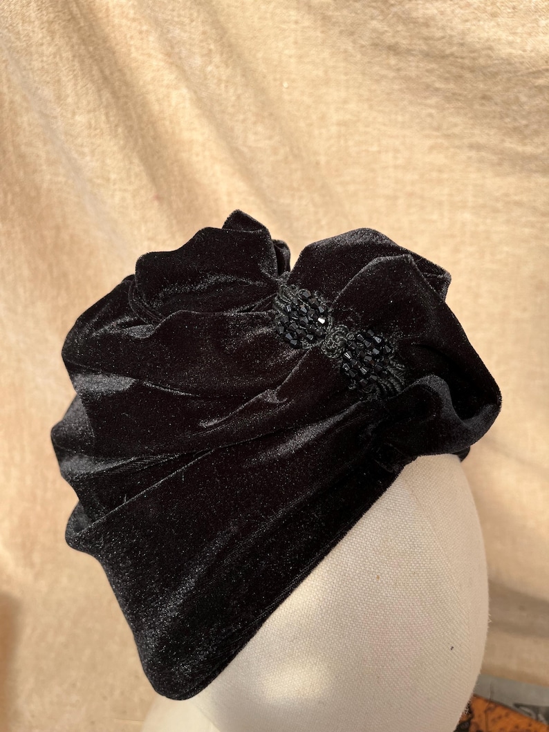May include: A black velvet hat with a large, ruffled bow and a black beaded embellishment.