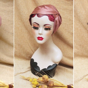 May include: A pink satin hat with a bow on the side. The hat is on a mannequin head with a black stand.