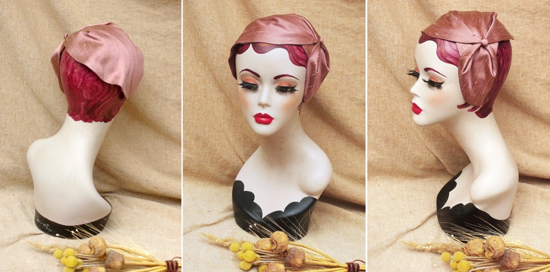 May include: A pink satin hat with a bow on the side. The hat is on a mannequin head with a black stand.