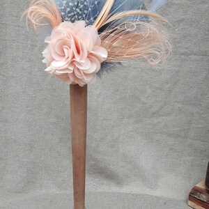 Peut inclure: Une fleur en tissu de couleur p&ecirc;che avec un filet &agrave; motifs bleus et blancs et des plumes attach&eacute;es &agrave; une base en bois.