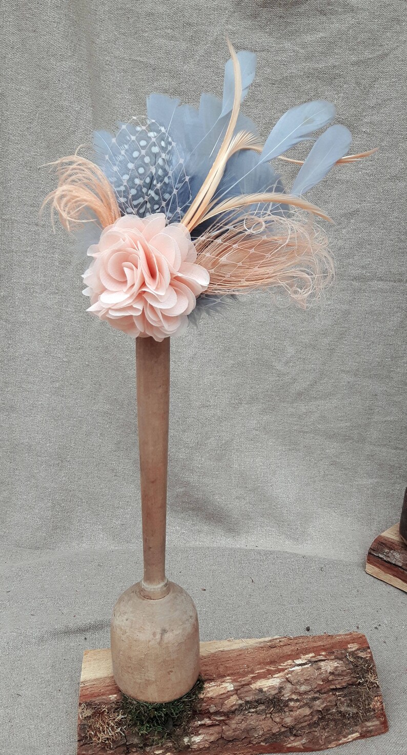 Peut inclure: Une fleur en tissu de couleur p&ecirc;che avec un filet &agrave; motifs bleus et blancs et des plumes attach&eacute;es &agrave; une base en bois.