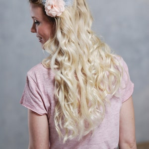 Peut inclure: Une femme avec de longs cheveux blonds boucl&eacute;s portant un t-shirt rose et une jupe grise. Elle porte une barrette de cheveux en forme de fleur bleu clair et rose avec des plumes.