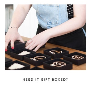 May include: Several small black square gift boxes arranged on a wooden surface, each containing a unique wooden ornament or jewelry piece. The text NEED IT GIFT BOXED? is displayed below the boxes, which feature various shapes including hearts and circles.