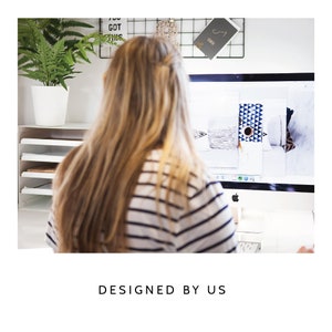 May include: A white computer monitor displaying various pillow designs, positioned on a desk with a white paper organizer and a green potted plant. The text "DESIGNED BY US" is printed in black capital letters below the image.