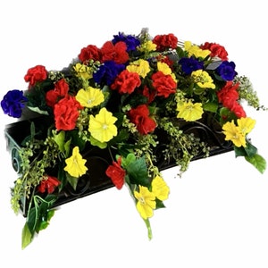 May include: A window box planter overflowing with a variety of colorful artificial flowers. The flowers are red, yellow, blue, and purple. The planter is made of metal and has a decorative design.