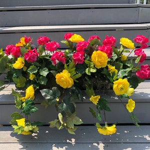 May include: A flower arrangement with pink and yellow flowers in a planter. The planter is sitting on a set of gray wooden steps.