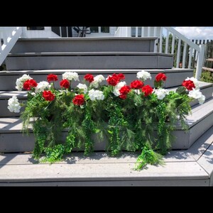 May include: A floral arrangement with red and white carnations and green foliage, spelling out the word "LOVE" on a wooden surface.