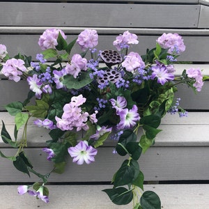 May include: A purple and green floral arrangement with a variety of flowers, including hydrangeas, petunias, and small purple flowers. The arrangement is on a set of gray wooden steps.