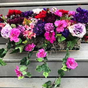 May include: A colorful floral arrangement in a rectangular planter with trailing pink flowers. The arrangement features a variety of flowers in shades of pink, purple, red, and white.
