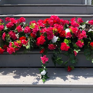 May include: A cascading arrangement of pink and white flowers in a planter on a set of gray wooden steps. The flowers are in full bloom and create a vibrant display.