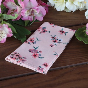 May include: A pink fabric napkin with a floral pattern. The napkin is folded and lying on a wooden surface.