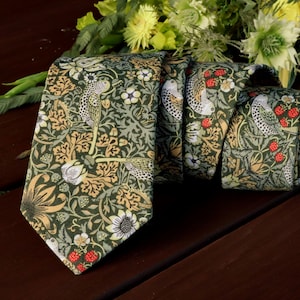 Può includere: Una cravatta verde con un motivo floreale e di uccelli. La cravatta presenta bacche rosse e fiori gialli.
