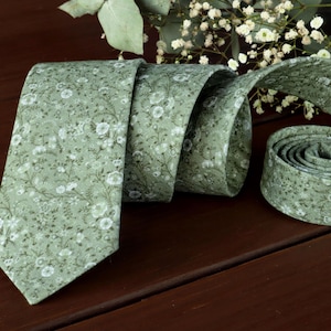 Peut inclure: Une cravate à motif vert avec des motifs floraux blancs. La cravate est pliée et nouée.