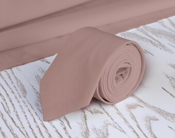 May include: A rolled up dusty rose colored tie on a white wooden surface.