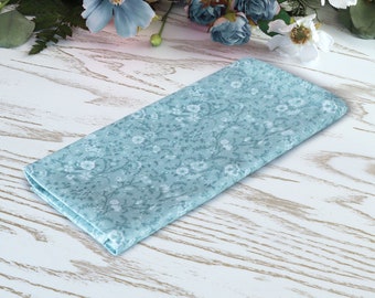 Può includere: Un tovagliolo rettangolare piegato, con un motivo floreale azzurro. Il tessuto presenta un delicato disegno di fiori e viticci bianchi, creando un'estetica morbida e vintage. Il tovagliolo è piegato con cura, pronto per l'uso.