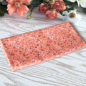 May include: A peach-coloured fabric with a floral pattern. The fabric is folded in half and has a white background with small pink and white flowers.